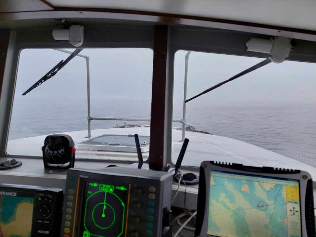 Kuvassa näkymä veneen sisäohjaamosta sumuiselle järvelle. Tutka ja karttaplotteri ovat käytössä.